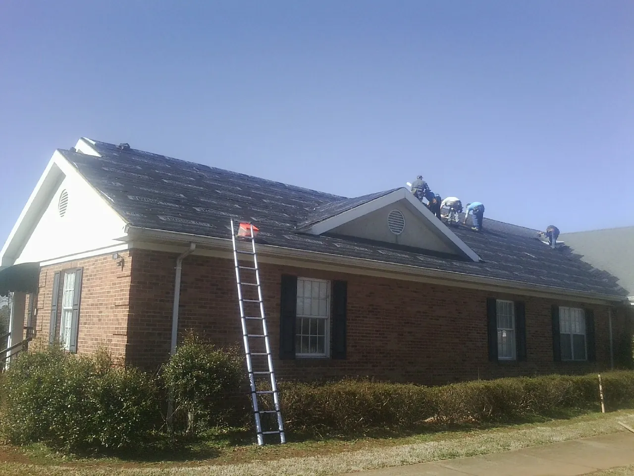 Crew tearing shingles off a brick ranch roof with a ladder set — Metal Roof Repair work by our crew in Joseph City