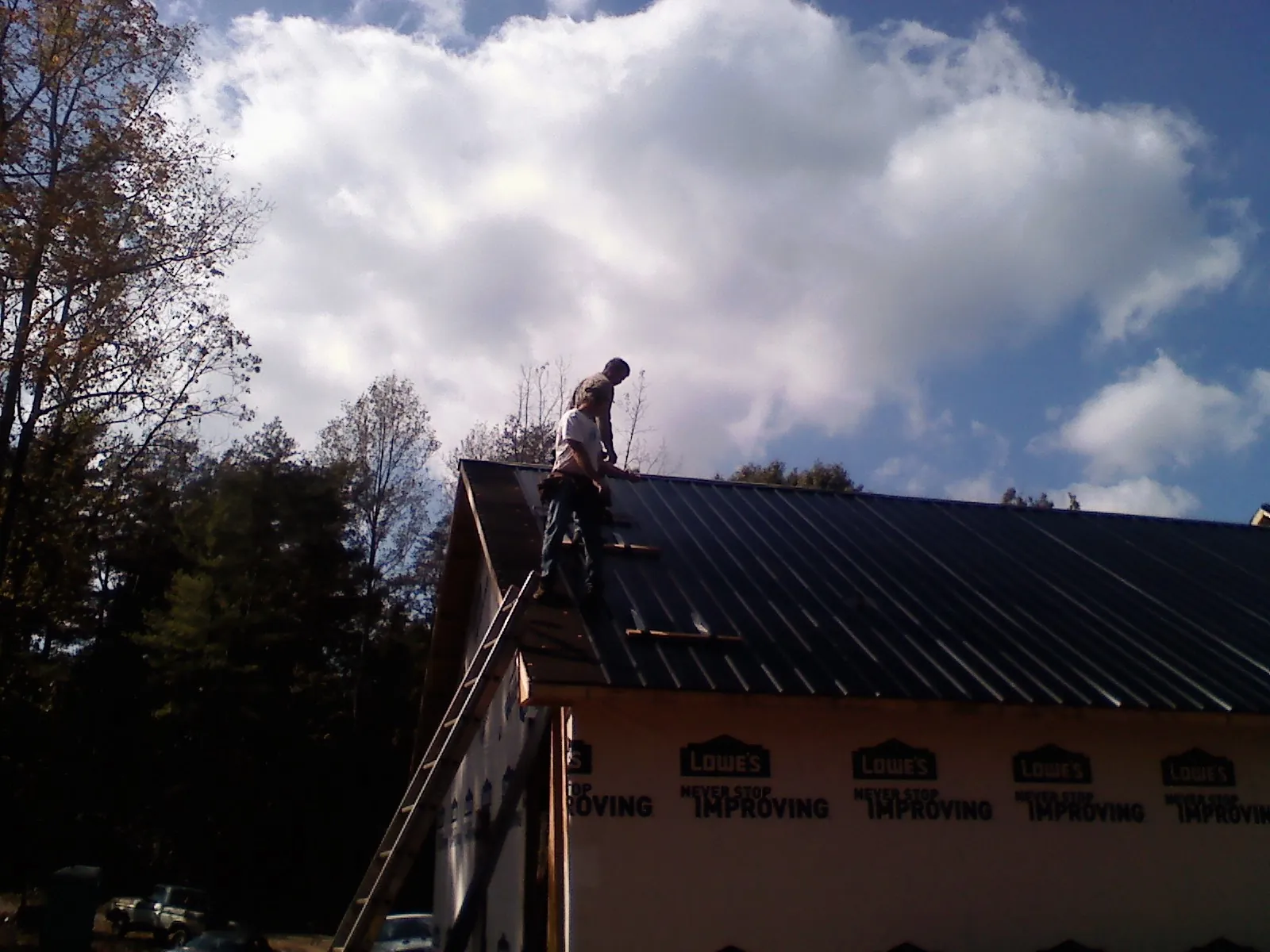 Roofer fastening dark metal panels high against a cloudy sky, from a Roof Inspection job in Joseph City