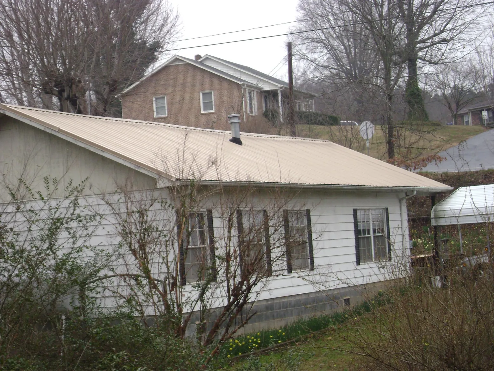 Tan metal roof on a white sided house set into a hillside — Commercial Roofing by Roofing Brothers in Joseph City